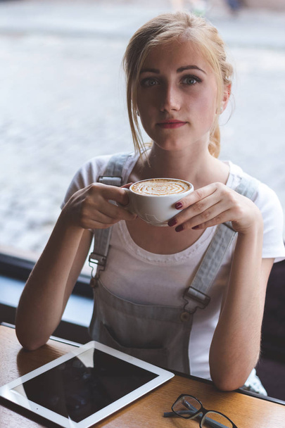 Enjoying coffee break. Top view of beautiful young woman holding cup of cappuccino while relaxing in cafe. - Foto, Imagem