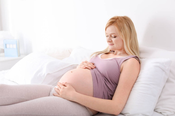 Beautiful pregnant woman resting on bed in light room - Foto, Bild
