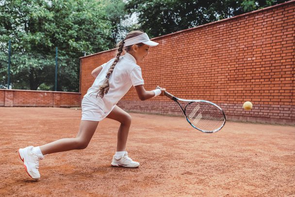 Child playing tennis on outdoor clay court. Full length shot of a tanned little girl on tennis court. Girl child playing tennis against the wall. Summer activities for children. - Photo, Image