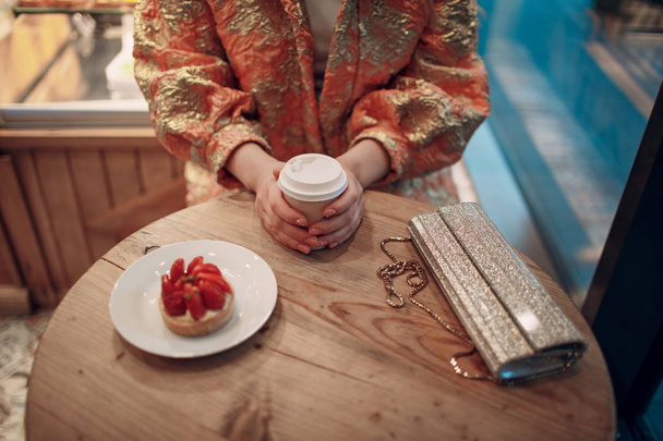 Nuori nainen istuu kahvilassa kahvin ja kakun kanssa.
. - Valokuva, kuva