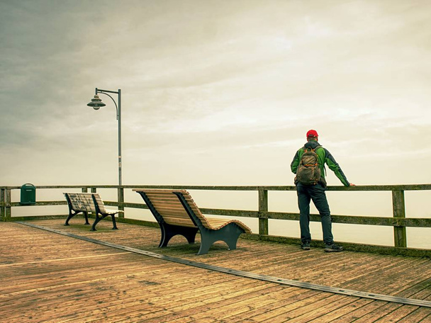Homem sonhando sentado em um cais de madeira perto da água e olhando para o horizonte distante
 - Foto, Imagem