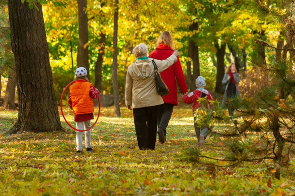 The grandmother shows something to her family, who is walking in the autumn yellow sunny park. - Fotoğraf, Görsel