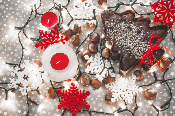 Kerst ontbijtkoek op de bruine feestelijke achtergrond omringd met kerstverlichting en noten - Foto, afbeelding