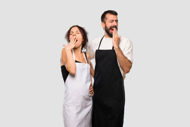 Couple of cooks yawning and covering mouth with hand. Sleepy expression on grey background - Photo, Image