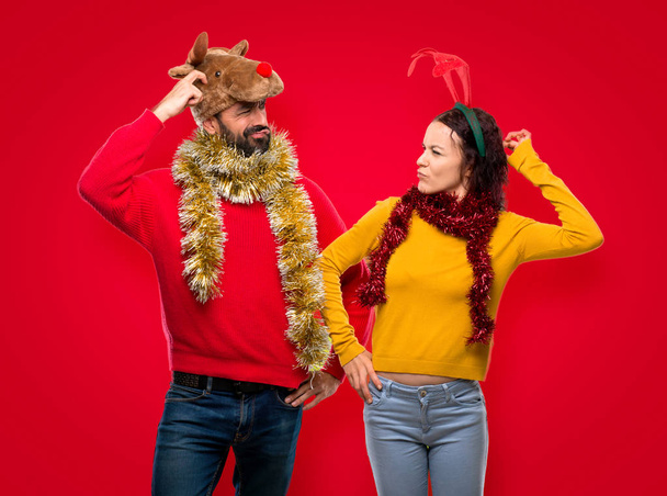 Pár oblečená pro vánoční svátky, pochybnosti a s tváří zmást při poškrábání hlavu na izolované červeném pozadí - Fotografie, Obrázek