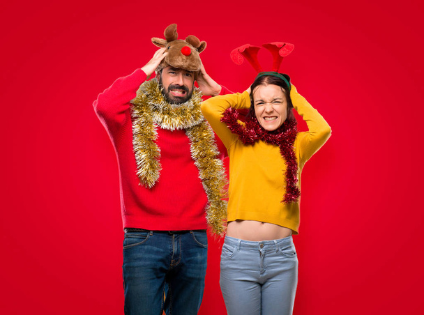 Paar verkleidet für die Weihnachtsfeiertage nimmt die Hände auf den Kopf, weil Migräne auf isoliertem roten Hintergrund hat - Foto, Bild