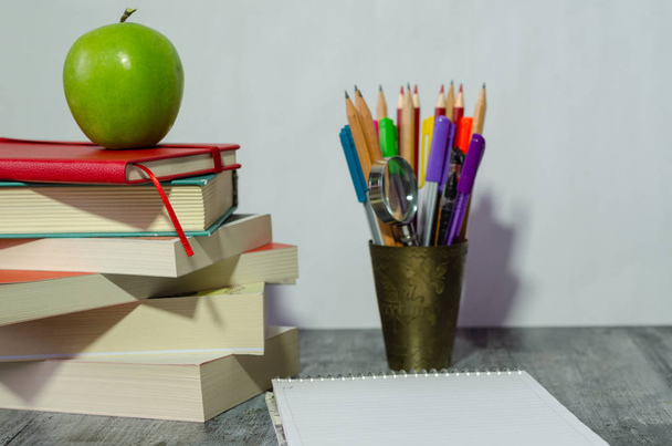 Βιβλία, μολύβια, το σημειωματάριο και το μήλο στο γραφείο, λευκό φόντο. - Φωτογραφία, εικόνα
