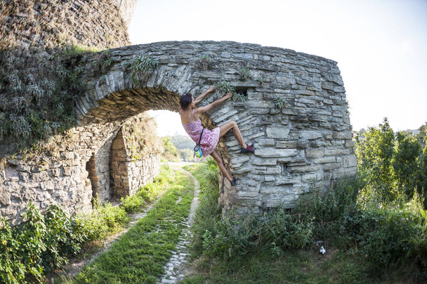 A lány mászik a kőfal. Egy nő, egy nyári ruha felmászik a falon egy régi elpusztult épület. Tégla kerítés. A mászó lógnak a város-épület. A romos vár megerősítése. - Fotó, kép