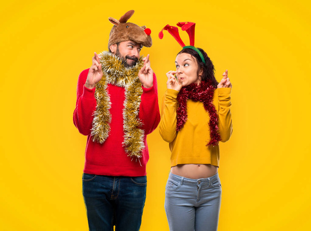 Paar verkleed voor de kerstvakantie met vingers oversteken en ik wens het beste op gele achtergrond - Foto, afbeelding