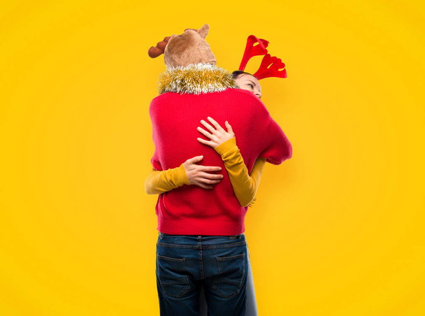 Paar verkleed voor de kerstvakantie knuffelen op gele achtergrond - Foto, afbeelding