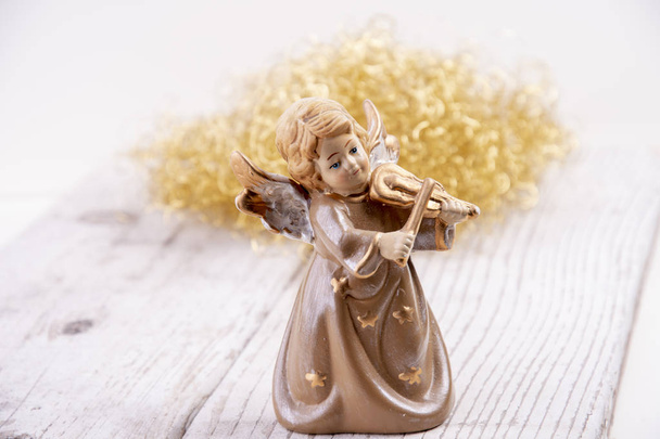 Ángel con violín delante de pelo dorado sobre madera blanca como fondo navideño
 - Foto, Imagen
