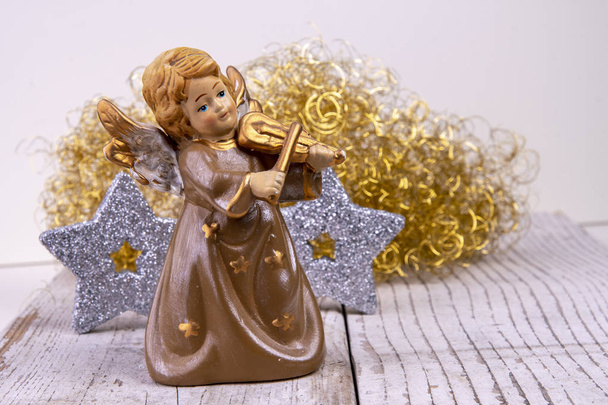 Άγγελος με βιολί μπροστά από χρυσά μαλλιά και ασημένια αστέρια στον λευκό ξύλο ως φόντο χριστουγεννιάτικο - Φωτογραφία, εικόνα