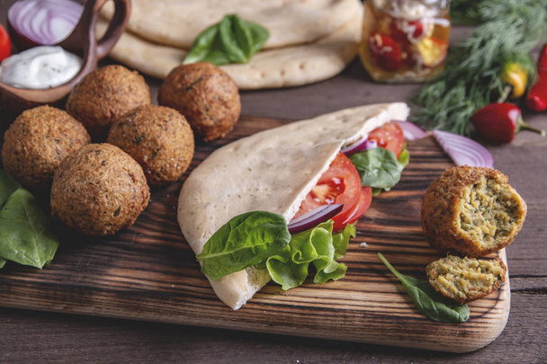 Falafel, fresh vegetables ,sauce and pita bread on wooden table - Photo, Image