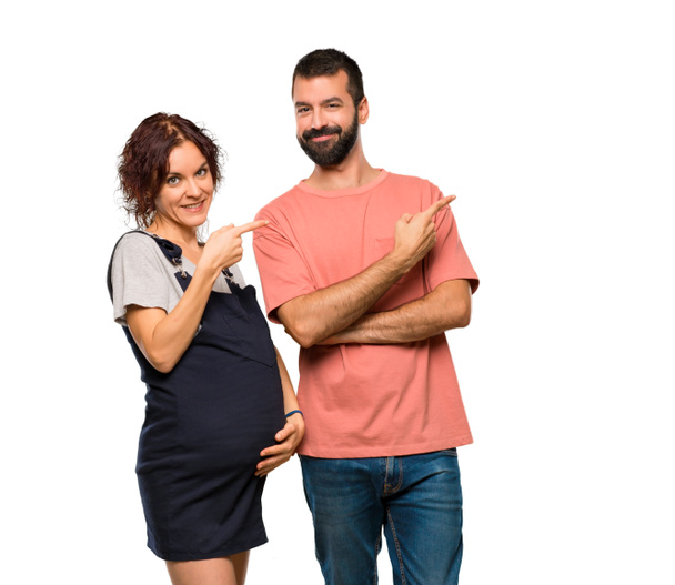 Couple with pregnant woman pointing to the side with a finger to present a product on isolated white background - Foto, immagini