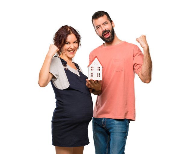 Пара з вагітною жінкою тримає маленький будинок на ізольованому білому тлі
 - Фото, зображення