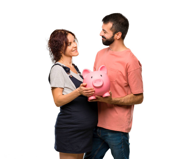 Couple with pregnant woman holding a piggybank on isolated white background - Valokuva, kuva