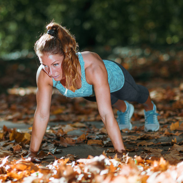 Woman doing push ups in the park, in the fall. - Photo, Image