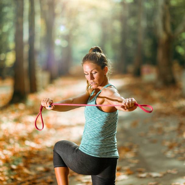 Woman Exercising With Elastic Band Outdoors in The Fall Public Park - Foto, immagini