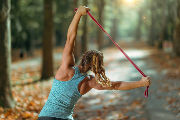 Woman Exercising With Elastic Band Outdoors in The Fall Public Park - Photo, Image