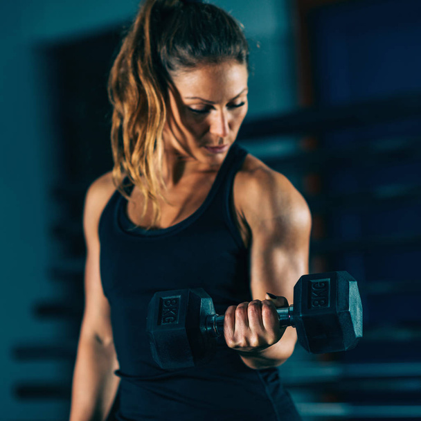 Cross training. Young woman exercising with dumbbell - Photo, Image