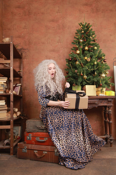 hermosa rubia en un vestido largo de leopardo posando en su habitación marrón con un árbol de Navidad
 - Foto, imagen