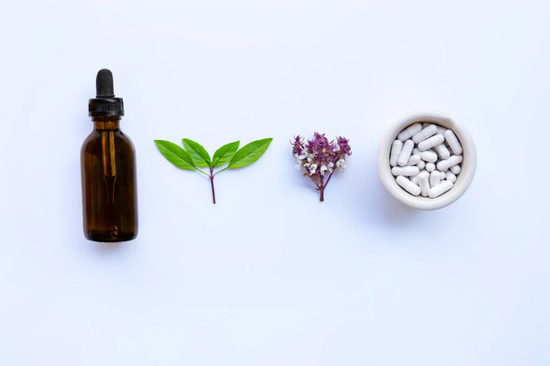 Sweet basil with drop bottle of essential oil  and  herb capsules on white background. - Photo, image