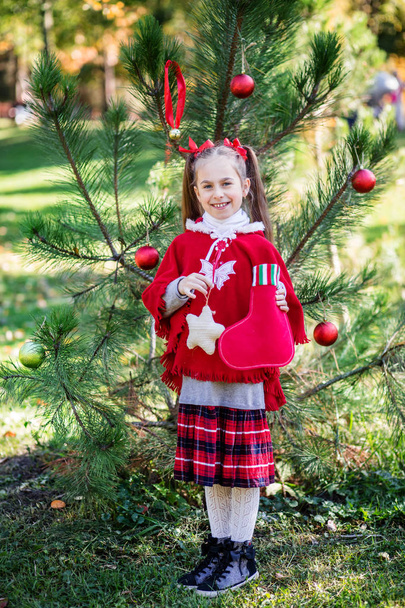 Aranyos lány díszíti a karácsonyfát, szabadban, az udvaron, az ünnepek előtt. Kellemes karácsonyi ünnepeket és boldog ünnepek. - Fotó, kép