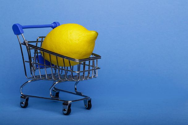 Lemon in shopping cart, shopping trolley on blue background - Foto, afbeelding