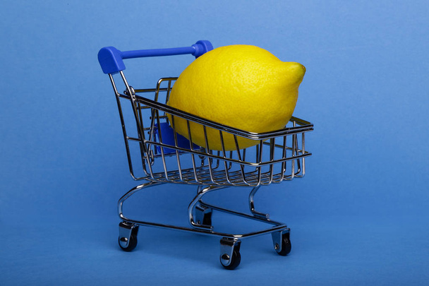Lemon in shopping cart, shopping trolley on blue background - Foto, imagen