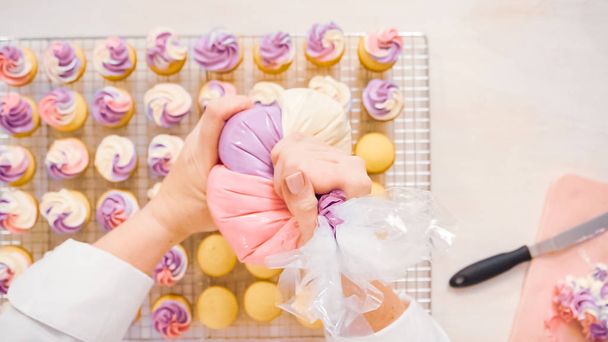 Flat lag. Roze en paarse botterroom glazuur leidingen op kleine vanille cupcakes. - Foto, afbeelding