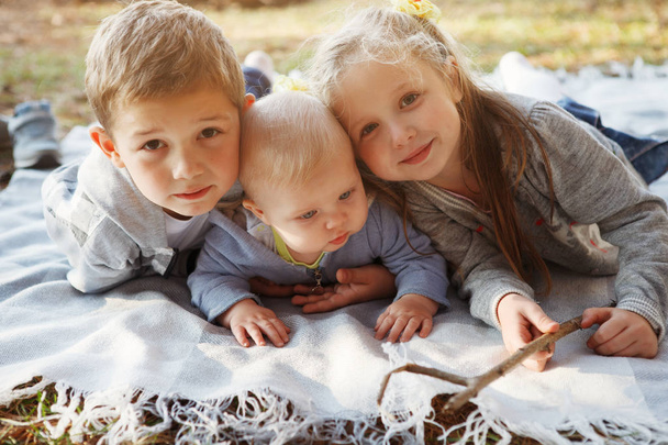 Trois enfants, frère aîné, sœur blonde et garçon de 7 mois aux yeux bleus sont couchés sur un tapis dans la forêt d'automne
. - Photo, image