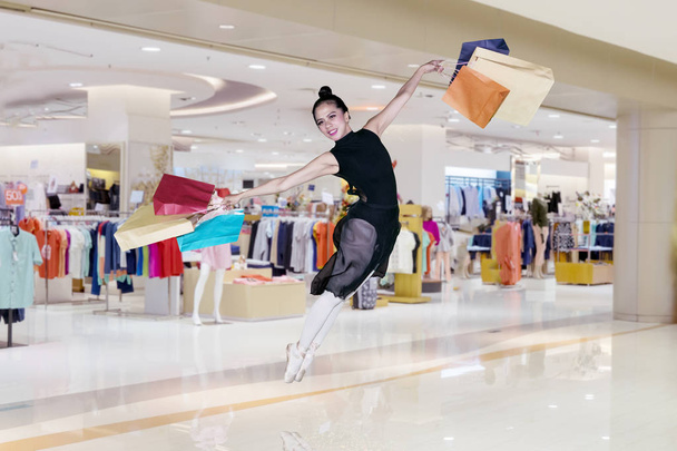 Portrait of beautiful ballerina is carrying shopping bags while leaping in the mall - Fotoğraf, Görsel