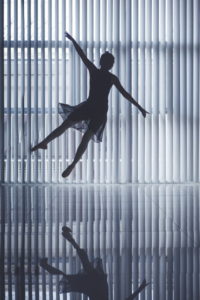 Silhouette of a graceful ballet dancer jumping and dancing near the window - Fotó, kép