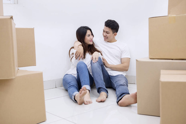 Image of happy Asian couple sitting with a stack of cardboard boxes in the new house - Valokuva, kuva