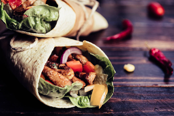 Traditional mexican tortilla wrap with vegetables and grilled chicken meat on dark wood table - Fotoğraf, Görsel