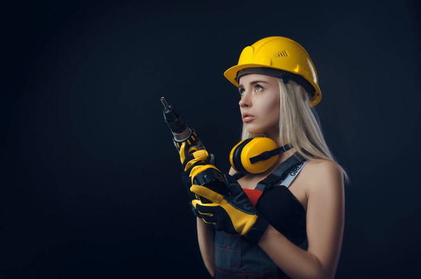 the girl in construction clothes and protective equipment posing with a screwdriver - Fotó, kép