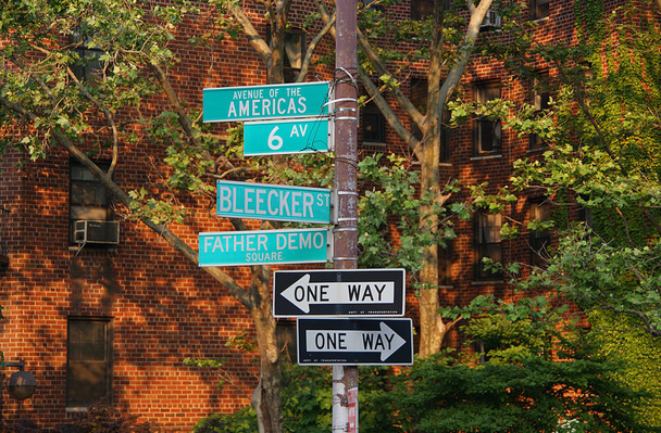 Panneau indiquant Avenue of the Americas, 6th Ave, Blecker Street, Father Demo Square, direction flèche unidirectionnelle avec des bâtiments et des arbres en arrière-plan sur Manhattan, New York, États-Unis. (2009)
) - Photo, image