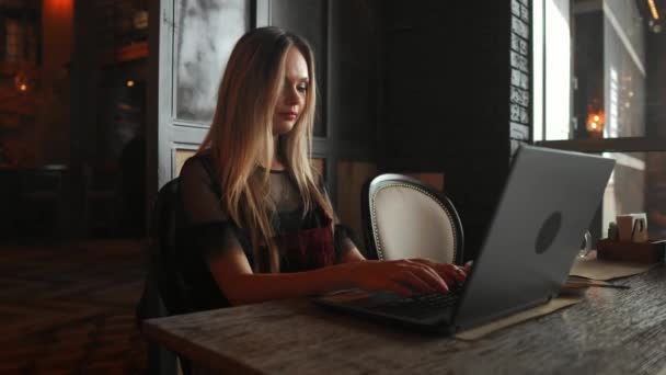 Πλαϊνή όψη. Νεαρή γυναίκα που κάθεται στο τραπέζι και σημειώσεις στο Σημειωματάριο. Στο τραπέζι είναι laptop, το smartphone και το φλιτζάνι του καφέ. Στον υπολογιστή οθόνη γραφικά και γραφήματα. Φοιτητής Μαθαίνοντας διαδικτυακά. Blogger. - Πλάνα, βίντεο