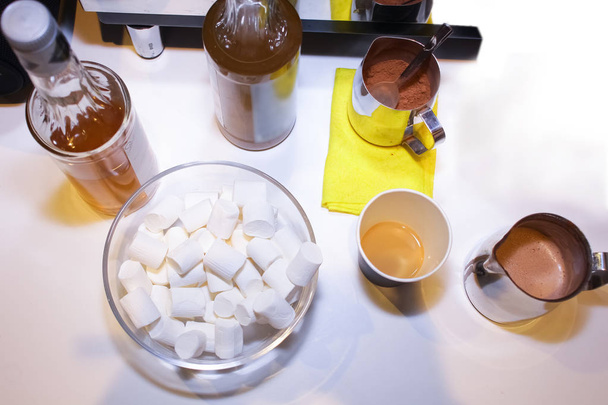 Glass transparent plate filled to the top with Bilan airy marshmallow and cups of hot cocoa. - Foto, afbeelding