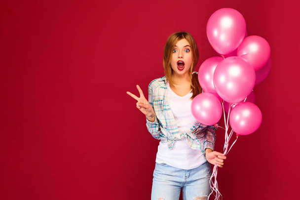 トレンディな夏のポーズに興奮若い女の子シャツ服のトップチェッカー。赤の背景にピンクの気球の女性モデル。聖女子日新年あけましておめでとうございます、誕生日パーティ - 写真・画像