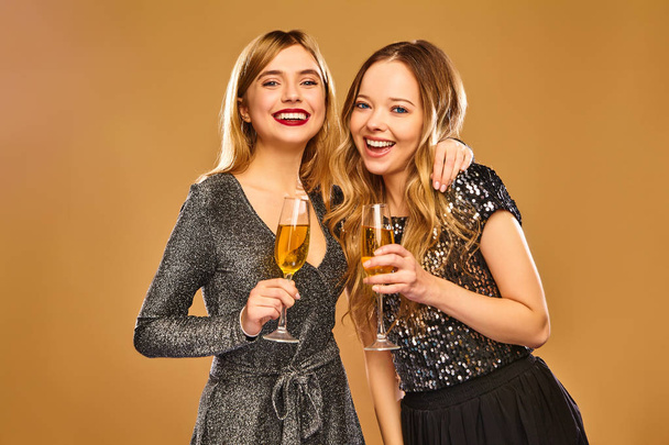 Beautiful blond women celebrating New Year.Models having fun at fashion party.Happy smiling girls in stylish glamorous dresses with champagne glasses. Isolated on golden background - Foto, Bild