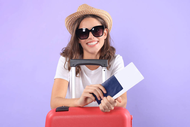 Young tourist girl in summer casual clothes, with sunglasses, red suitcase, passport isolated on purple background - Foto, afbeelding
