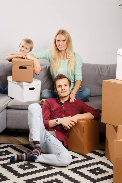 Image of woman and boy sitting on couch, men sitting on floor among cardboard boxes - 写真・画像