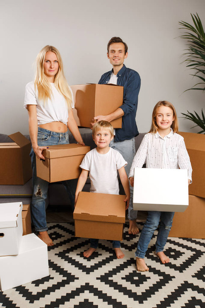 Full-length picture of young married couple with children with cardboard boxes in their hands standing - Photo, image