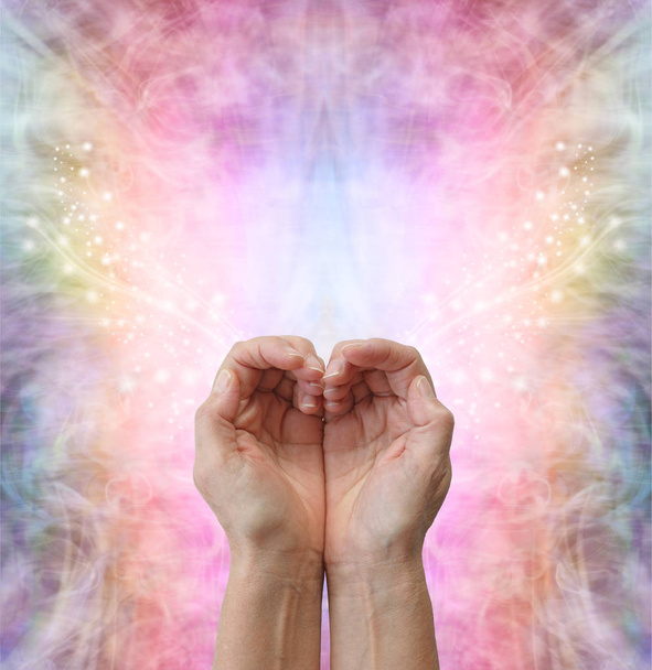 Healers hands making a humble heart shape - female hands in open cupped position creating a heart shape on a rainbow coloured sparkling energy formation background  with copy space above - Photo, Image
