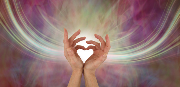 Отправка любовных вибраций - женские руки, создающие форму сердца с потоком энергии, текущей с обеих сторон на теплом многоцветном эфирном фоне и копирующем пространстве
 - Фото, изображение