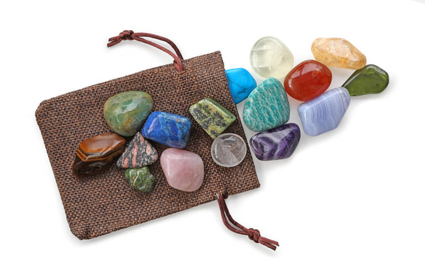 La preciosa bolsa de piedras de colores de Crystal Healer - Una selección de 16 diferentes piedras en tambor Crystal Healing colocadas en una bolsa de regalo marrón aislada sobre un fondo blanco
 - Foto, imagen