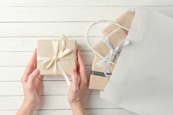Руки жінки обгортають подарунки в подарунковій сумці на білому тлі, вид зверху
 - Фото, зображення