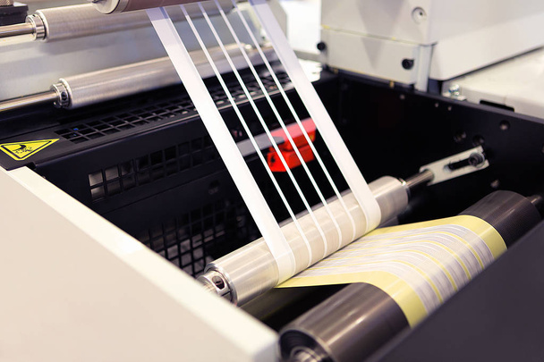 Close-up shot of labels manufacturing on flexo printing machine. Photo detail of matrix waste or trim removal from adhesive material on flexographic press. - Zdjęcie, obraz
