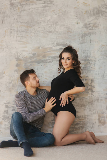 Happy man put his handr on the belly of his pregnant wife. Young family in studio. Couple wait for a baby - Foto, imagen
